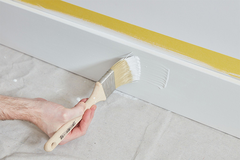 Image of a person using a paint brush to cut in a baseboard