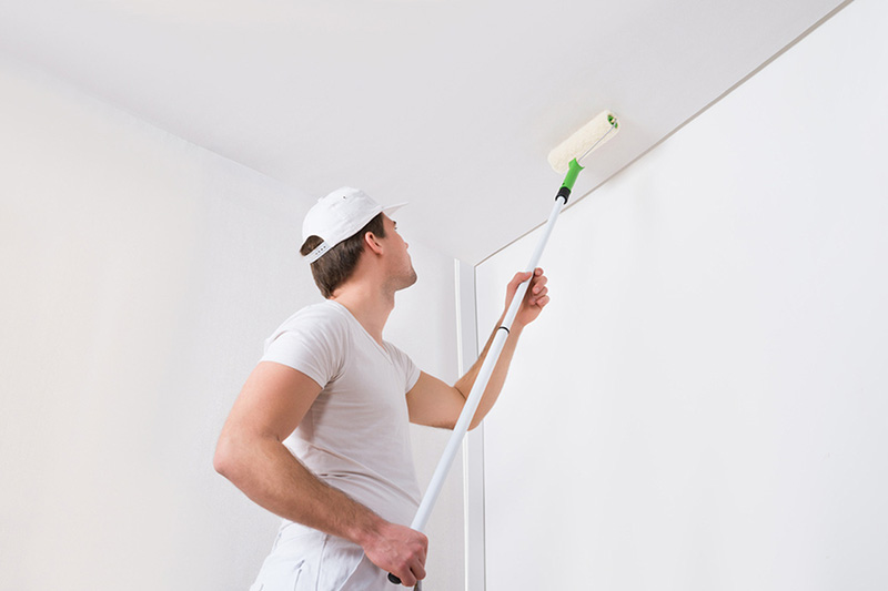 Image of a painter spraying a fresh coat of paint on a ceiling.