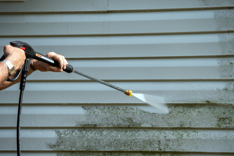 Image of a person power washing a wall covered in siding