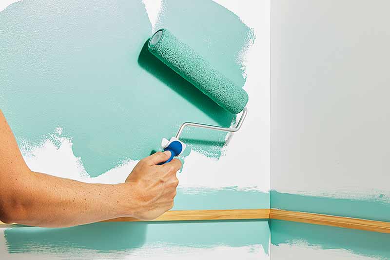 Image of a person painting a wall using a roller brush