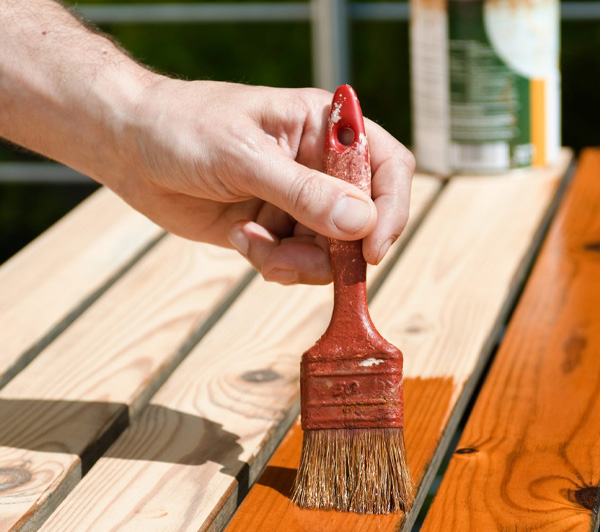 Image of person applying a brown stain to a deck