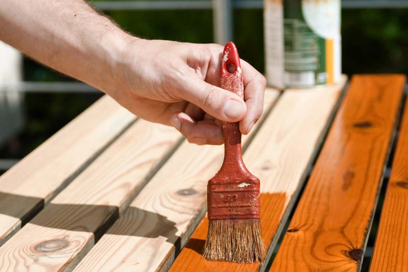 Image of person applying a brown stain to a deck