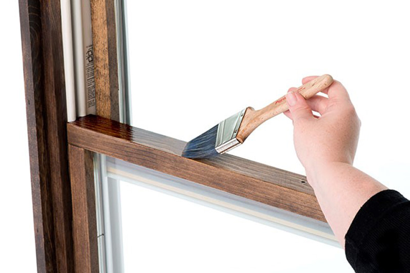 Image of someone applying dark stain to a window frame
